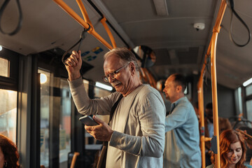 En elderly man standing in a bus looking at his phone