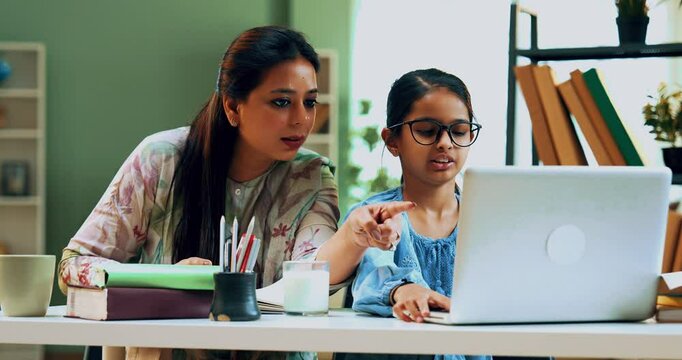 Indian Asian attentive, smart secondary school girl studying on laptop while her caring mother sits beside her in a lavish home, both looking at the camera with a warm smile
