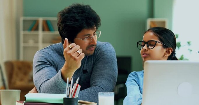 Indian Asian school girl using a laptop for studies while father sits beside, guiding, helping with homework in modern lavish home, fostering online education, digital learning, and academic success