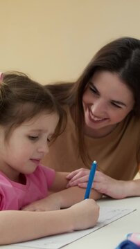 Happy brunette girl teaching homework with her little daughter child at home
