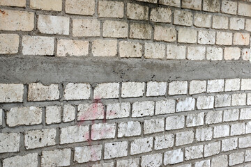 A pale white brick wall is neatly arranged with gray cement layers between the bricks, displaying a rough texture and a repeating rectangular pattern