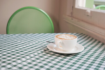 Coffee cup placed on a green checkered tablecloth in a cafe