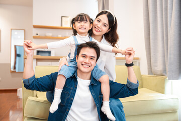 Happy family portrait: Father giving piggyback ride to his daughter while mother smiles nearby