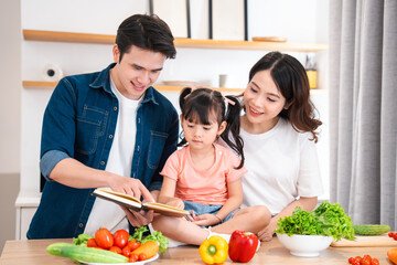 Family enjoys looking at a recipe book while preparing a fresh salad with various vegetables