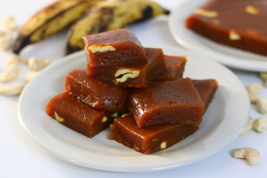 Sliced banana halwa in a tray, shot along with ripe bananas