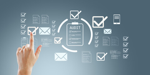 Hand touching digital audit checklist icons on transparent interface with abstract business symbols on blue background conceptually representing review process.