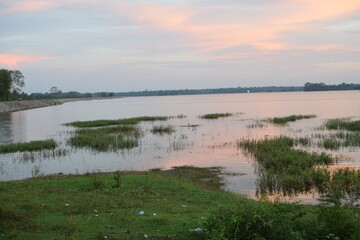 Fototapeta premium On a lake embankment at sunset. nature with lake landscape on sunset time. Cloudy Sunsets Over Lake in Summer. chandrika lake, Embilipitiya, Sri Lanka. Golden Sunset Reflections on Lake’s Tranquil
