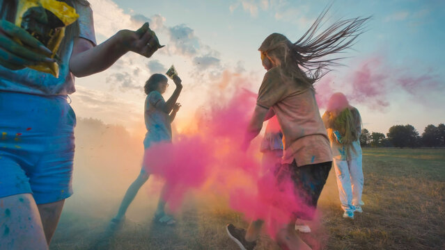 Young people celebrating holi festival, throwing colored powder at sunset, having fun together