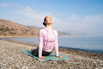Woman stretching in cobra pose on fitness mat on the beach. Flexible girl athlete practicing yoga,...