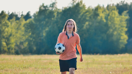 Fototapeta premium Student strolling through a grassy field with a soccer ball, soaking up the sunshine after school