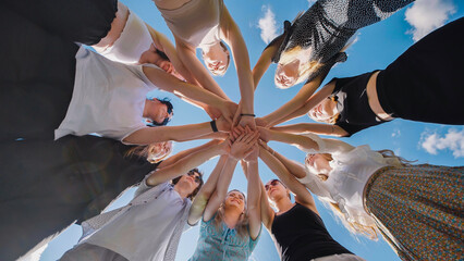 Group of young people is standing in a circle joining their hands in the center, symbolizing their strong bond and friendship