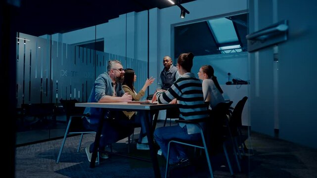 A diverse team of young professionals collaborates in a modern office conference room. Businesspeople discuss strategy, technology, and planning, using laptops to develop an innovative e-commerce