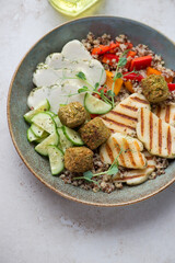 Rustic plate with halloumi cheese, falafel, quinoa and vegetables, vertical shot on a light-beige stone background, elevated view, middle closeup