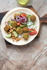 Flat bread with falafel, yogurt and fresh vegetables, vertical shot on a brown granite background with space, above view
