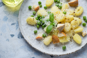 Closeup of potato gnocchi with different types of cheese, green peas and basil on a grey plate, horizontal shot