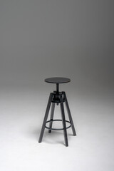 A black industrial-style stool with a round adjustable seat and four sturdy legs stands against a...
