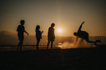 Fototapeta premium A group of friends enjoying a sunset at the beach, silhouetted against the evening sky. Their relaxed poses and playful actions convey a sense of freedom, fun, and togetherness.