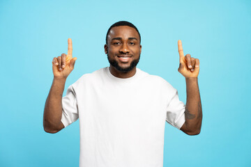 Smiling African American man pointing up with index fingers on blue background