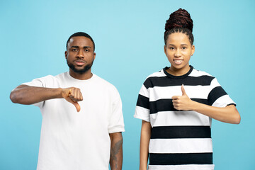 Sad man and positive African American woman showing opposite thumbs up and thumbs down gestures