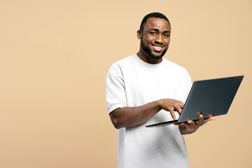 Smiling African American man using laptop on beige background