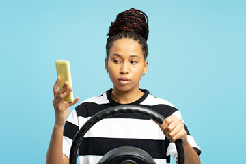 Serious African American woman driving and using mobile phone against blue background
