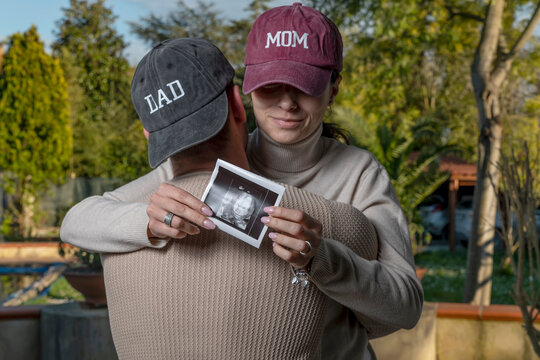 A pregnant woman hugs her man holding an x-ray of her unborn baby - Powered by Adobe