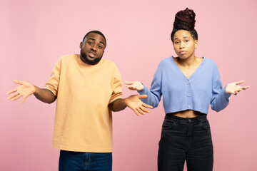 Confused African American couple shrugging shoulders on pink background