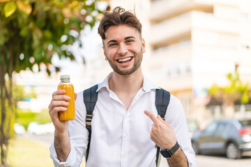 Young handsome man holding an orange juice at outdoors with surprise facial expression