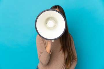 Young caucasian woman isolated on blue background shouting through a megaphone to announce something