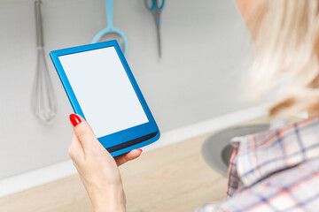 woman reading e-book in kitchen at home. housewife reading e-book. ebook mockup. place for inscription. modern blue e-book. reading book in the kitchen. 