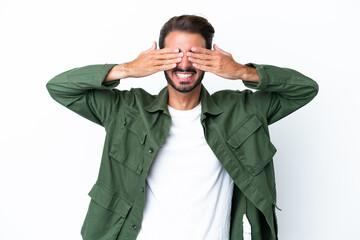 Young caucasian man isolated on white background covering eyes by hands and smiling