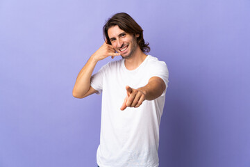Naklejka premium Young handsome man isolated on purple background making phone gesture and pointing front