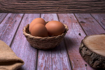 three chicken eggs in a wicker basket on a rustic wooden table