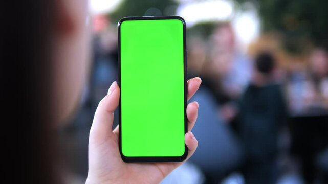 Person holding a green phone with a green screen. The phone is being held in a hand and the person is looking at it
