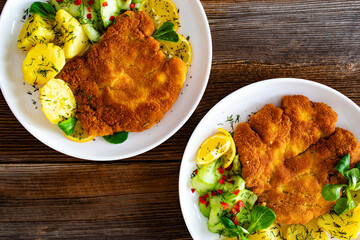 Crispy breaded seared chicken cutlet with boiled potatoes and fresh cucumbers served on wooden...