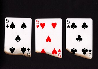 A hand of three burnt playing cards of the same value.