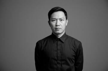 Obraz premium Black White Portrait Confident Adult Asian Male Formal Black Shirt Gray Background - Professionalism Corporate Branding Concept Business Development Leadership