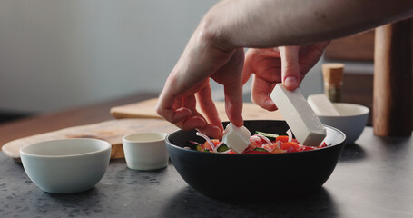 man put feta cheese into greek salad in black bowl
