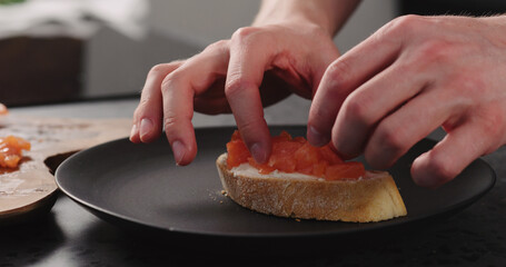 man hands making bruschetta with cream cheese and salted trout on black plate