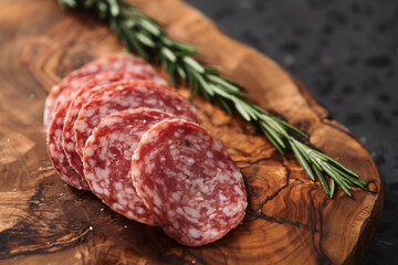 Sliced salame milano sausage on olive wood board with rosemary
