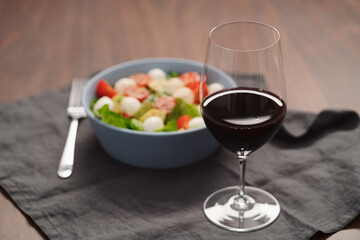 Glass of red wine with salad with romaine, tomatoes and mozzarella in blue bowl