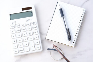 電卓とペン、メモ帳で家計をやりくりしているイメージ
