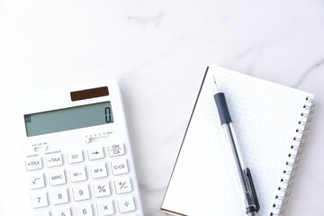 電卓とペン、メモ帳で家計をやりくりしているイメージ
