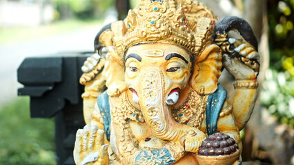 An old hindu stone statue of Ganesha covered with moss, standing on the street on the Bali