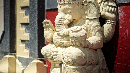 An old hindu stone statue of Ganesha covered with moss, standing on the street on the Bali