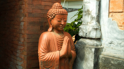 An old red clay statue of Buddha standing on the street on the bali