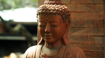 An old red clay statue of Buddha standing on the street on the bali