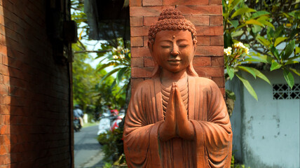 An old red clay statue of Buddha standing on the street on the bali