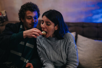 A couple enjoys their time together while sharing a snack on a relaxed evening indoors,...