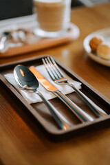 Cutlery placed neatly on a wooden tray ready for meal at a cozy cafe in the morning